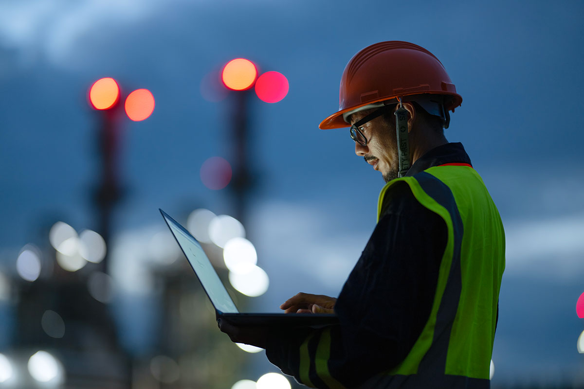 Gas facility engineer standing outside and looking at laptop
